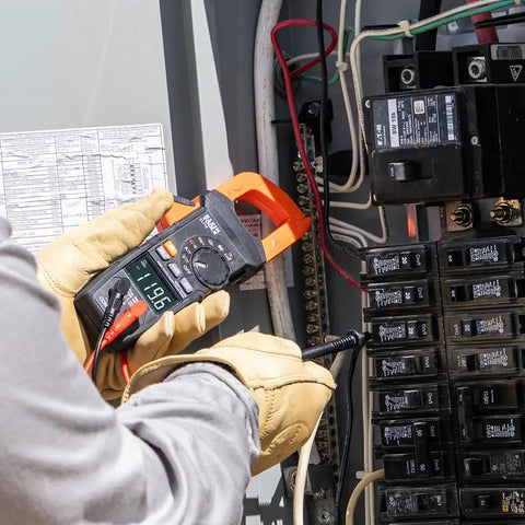 Electrician using Auto Ranging Digital Clamp Meter With True RMS for AC and DC current in electrical panel.
