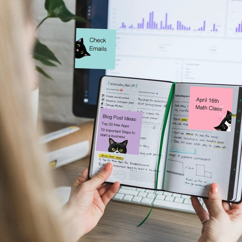 Person holding notebook with Nine Pad Cat Themed Sticky Notes Set In Pink With Super Adhesive Self Stick Notes on pages, monitor in background