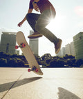 Skateboarder performing trick in urban setting with sunlight, showcasing orange wheels and deck