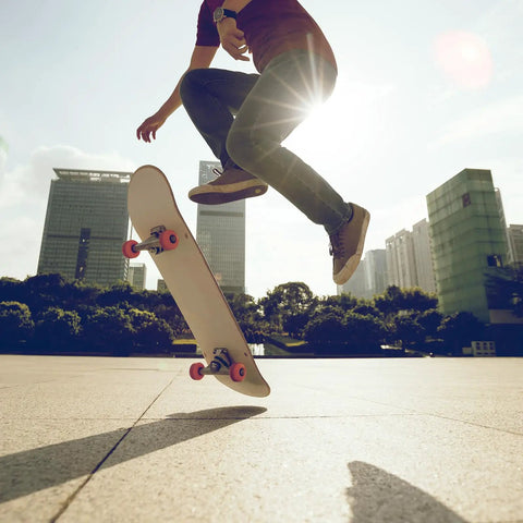 Skateboarder performing trick in urban setting with sunlight, showcasing orange wheels and deck
