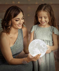 Mother and daughter admiring Moon Lamp 3D Printed Lunar Light With Black Stand 3.5 Inch Night Light USB Charging Touch Control Brightness Dual Warm And Cool White Real Moon Surface Inspired By NASA Photos Great Gift For Kids Women Girls Boy Birthday in a cozy setting.
