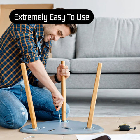 Side view of a man assembling a round gray metal table base with three wooden legs.