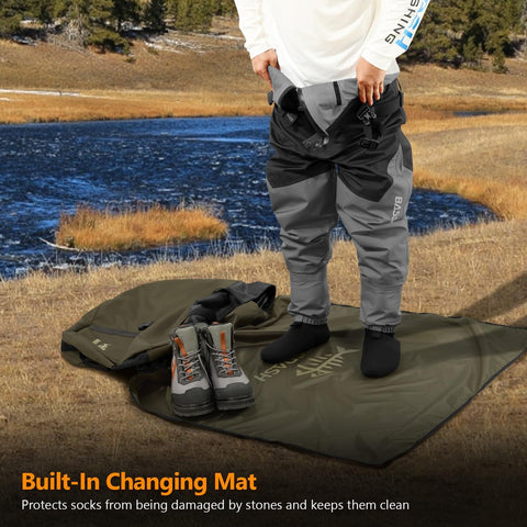 Person using Wader Bag Foldable With Changing Mat And Shoulder Strap For Fishing Travel And Hunting Waterproof Leak Proof Interior With PVC Coating Rugged 600D Ripstop Build And Mesh Boot Storage Built To Last beside a lake.