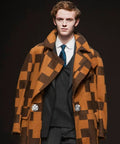 Model wearing a brown and black checkered coat with large lapels, over a white shirt and tie, fastened with snap buttons.