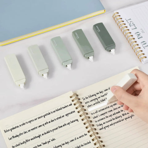 Hand using Six Pack Mini White Correction Tapes For Quick Corrections, Smooth Pull Out, Quick Dry, Aesthetic Cute Design For Students And Office Use, Easy To Use Set In Green on notebook