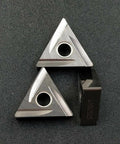 Two silver TNMG triangular carbide turning inserts with a central mounting hole; includes a dark NX25 piece