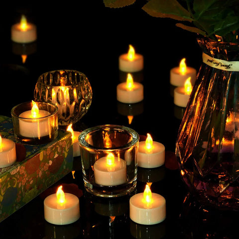 Flameless Tea Light Candles 50 Pack With Batteries Included Realistic Flickering LED Tealights on reflective surface with glass vases.