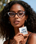 Third-Generation Lens Wipes packet held by a woman; 120-count, individually wrapped pre-moistened lens cleaner for glasses.