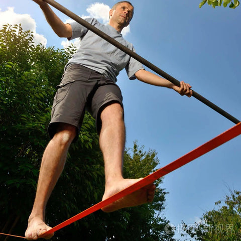 Man balancing on 65ft Ninja Slackline Kit With Ratchet System And Tree Protectors, 500lb Capacity Backyard Set