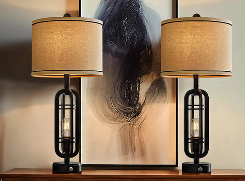 Set of 2 Industrial Black Table Lamps with USB Ports, beige shades, on wooden table against abstract art backdrop.