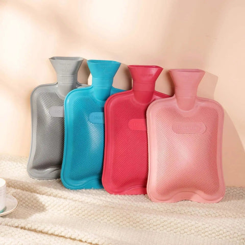 Four colored rubber hot water bottles lined up, with ribbed exteriors for heat retention. Premium Classic Rubber Hot Water Bottle Red For Cozy.