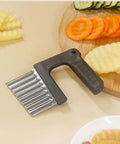 Angled view of stainless steel crinkle cutter with black ergonomic handle on a wooden cutting board.