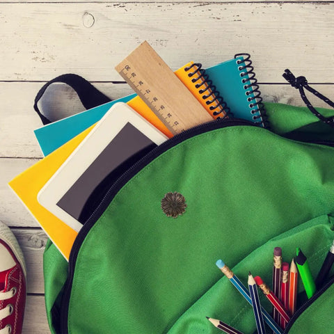 Top view of green backpack with tablet, notebooks, ruler, pencils, and a sneaker on wooden floor