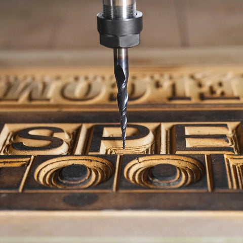 Close-up of a carbide end-mill bit with 1/8 in shank and tapered cone nose carving wooden letters.