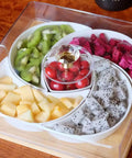Ceramic fruit tray with sections of kiwi, dragon fruit, and cherries topped with a crystal handle on a wooden table.