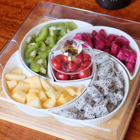 Ceramic fruit tray with sections of kiwi, dragon fruit, and cherries topped with a crystal handle on a wooden table.