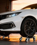 Heavy Duty Wheel Dollies Set Of 4 With Brakes 6000 Lbs Capacity High Tensile Steel Safe Lifting Rolling Under Load Built Tough For Daily Grind Beefy Workhorse Handles Loads Without Breaking Sweat Pro Shop Use Good For Mechanics Keep Garage Safe Now under white car on garage floor