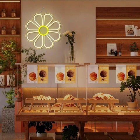 Flower Neon Sign Daisy Window Light LED Warm White for Bedroom Decor, above a bakery counter in a cozy room.