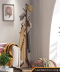 Freestanding Bamboo Coat Rack With 8 Hooks, holding coats and hats, classic brown, placed beside a sofa in a living room setting.