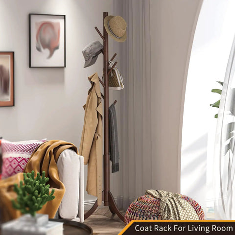 Freestanding Bamboo Coat Rack With 8 Hooks, holding coats and hats, classic brown, placed beside a sofa in a living room setting.