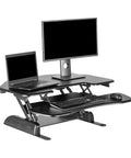 Cube Corner 36 Inch Standing Desk Converter for dual monitors with spring lift, shown with keyboard, mouse, and dual screens, black.