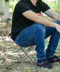 Person sitting on Portable Oxford Cloth Folding Stool Camping Chair With Sturdy Aluminum Frame in a forest setting.