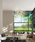 Straight Up 16 Light Satin Brass Foyer Pendant Chandelier With Real Clear Crystal Rods in modern living room with large windows.