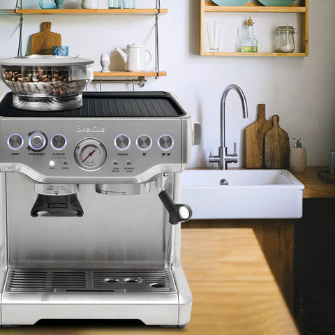 Breville espresso machine on a kitchen counter with a glass bowl of coffee beans on top