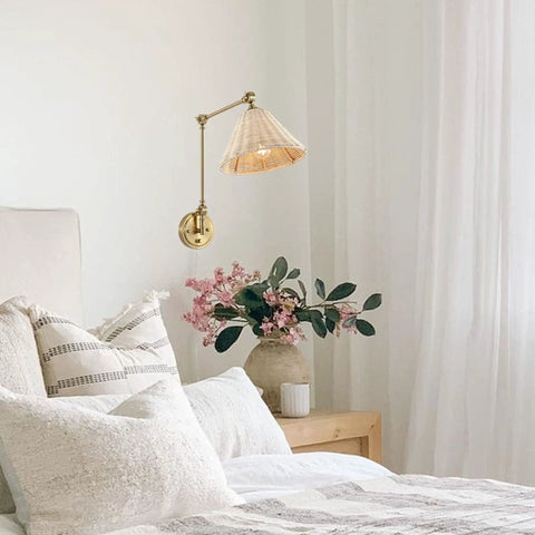 Rattan Wrapped Wall Sconce With Adjustable Swing Arm And Foldable Vintage Bedside Light Gold Finish With Wicker Shade Plug In Or Hardwire Brass Reading Lamp For Living Room Or Bedroom mounted above a bedside table with flowers