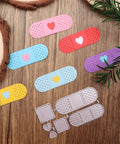 Colorful plasters with heart designs next to a metal cutting die set on a wooden surface