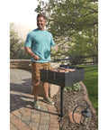 Man grilling sausages on Heavy Duty Park Style Charcoal BBQ Grill For Camping Backyard Patios And Tailgating in the sun.