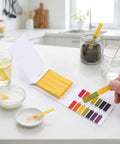 All Purpose Litmus Paper 1-14 Acid Test Strips Kit, Ten Pack For Wet Soap, Lemon Juice, Milk, Detergent, Wet Soil, Saliva, Sweat, And Aquarium Water Testing, Great For At Home Lab Use displayed on kitchen countertop with liquids.