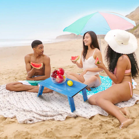 Ultralight Aluminum Mini Table With Adjustable Retractable Legs on beach, 66 lb capacity, used for picnic with watermelon and fruits.