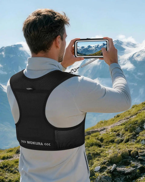 Man wearing Ultra Lightweight Hydration Vest For Running With 500ml Soft Flask in black, viewing mountain landscape through phone.