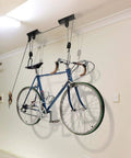 Ceiling Mount Bike Hoist Set Of 2 With Pulley System And Bike Hangers Easy Overhead Storage For Garage Or Workshop Holds Up To 55 Lbs Each Heavy Duty Rope Smooth Operation Space Saving mounted on ceiling holding a road bike