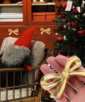 Hand holding Vintage Bow Shaped Dresser Knob in antique gold, in front of decorated cabinet and holiday setting.