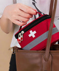 Person placing multilayer waterproof medical organizer bag in handbag, visible red design with cross symbol, easy carry handle