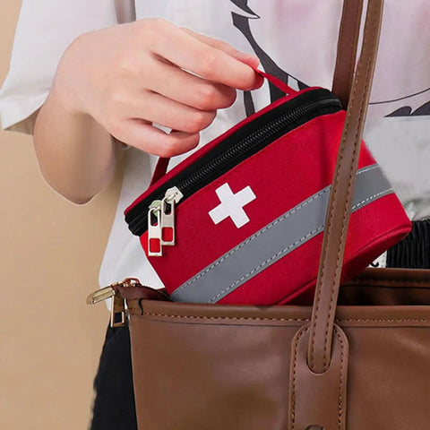 Person placing multilayer waterproof medical organizer bag in handbag, visible red design with cross symbol, easy carry handle