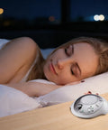 Sleeping woman beside SS-2000 White Noise Sound Machine Charger and Replacement Power Adapter, 6V DC 300mA Output on nightstand.
