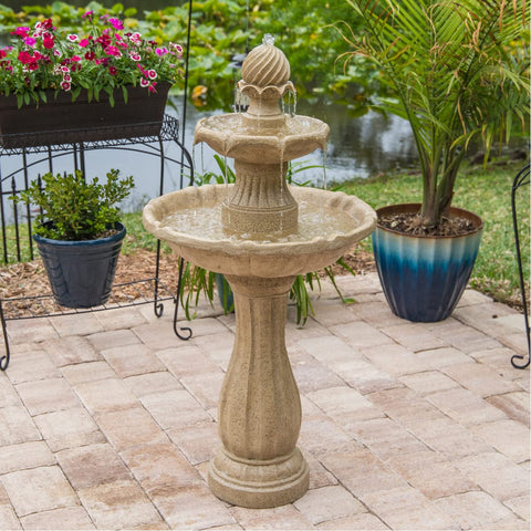 Stone garden fountain with two-tier design on patio near plants and pond