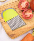 Crinkle cutter knife with lime-green handle and stainless steel comb-blade on wooden cutting board beside tomatoes