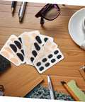 96 Piece Eyeglass Nose Pads Adhesive Cushions For Glasses Nonslip Comfort Comfy EVA Sponge Nose Pads on table with glasses and coffee.