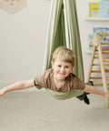 Child in Ultimate Chill Cotton Sensory Cocoon Swing For Kids Autism And Adhd Therapy Support Indoor, fabric in desert sage.