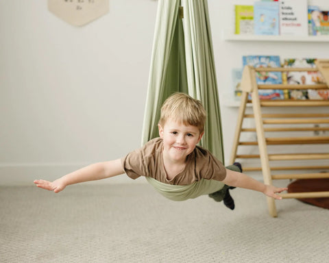 Child in Ultimate Chill Cotton Sensory Cocoon Swing For Kids Autism And Adhd Therapy Support Indoor, fabric in desert sage.
