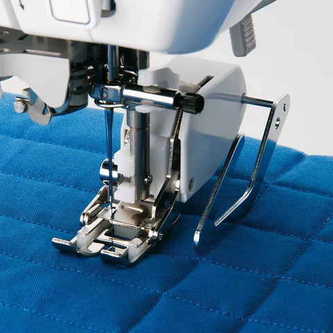 Front view of sewing machine needle area with universal quilting guide bar on presser foot over blue quilted fabric.