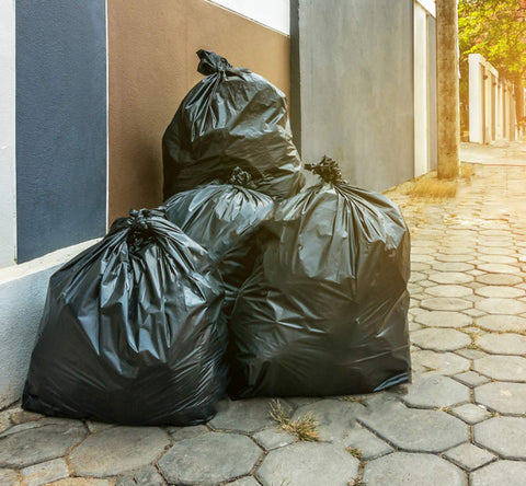 Heavy Duty Sixty Four Gallon Trash Bags Black Garbage Containers Value Pack Of Fifty with secure tie tops piled on sidewalk.