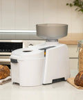 Beefy 1200W High Speed Electric Grain Mill for Fresh Flour next to bread on a kitchen counter.