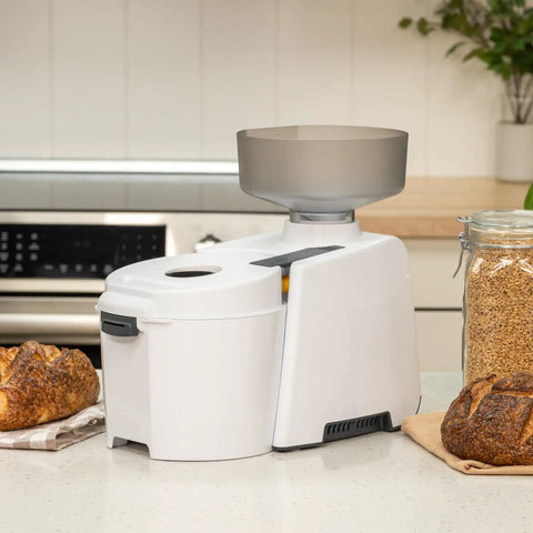 Beefy 1200W High Speed Electric Grain Mill for Fresh Flour next to bread on a kitchen counter.