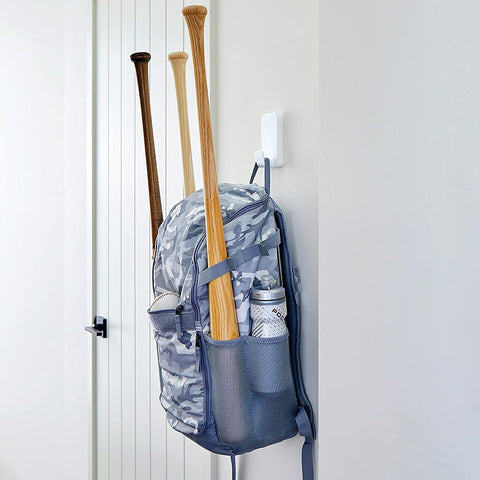 Extra Large Heavyweight Wall Hooks With Adhesive Strips holding a backpack with baseball bats hanging on a smooth wall.