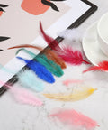 Various colorful feathers on a table, including dark blue rooster saddle hackle feathers, suitable for crafts and decorations.